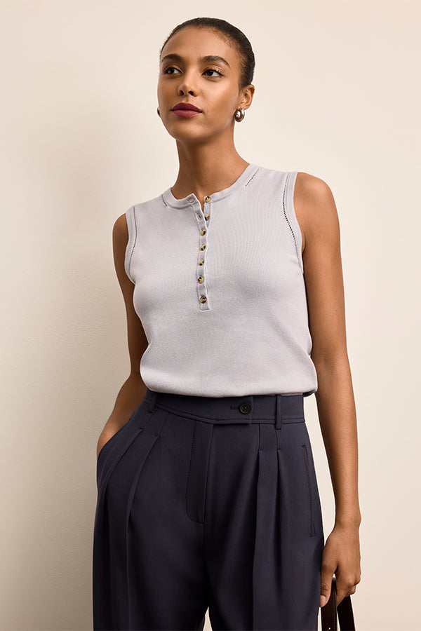Woman wearing a light gray sleeveless top with buttons and dark blue pants against a beige background | Exclude | Grid