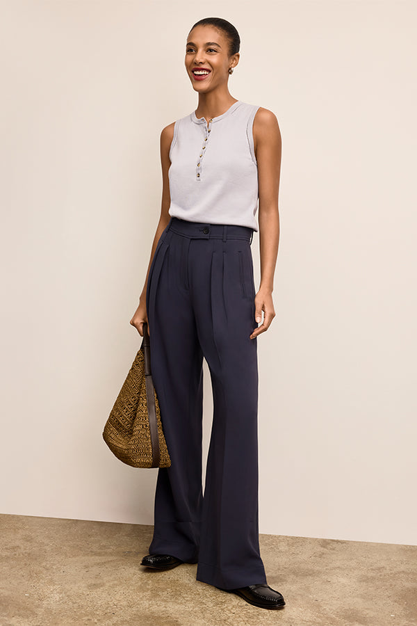 Woman wearing a sleeveless top and wide-leg pants, holding a bag against a plain background | Exclude | Grid Hover
