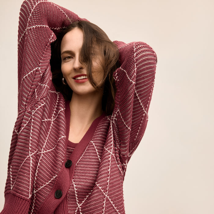 Woman wearing a maroon knitted cardigan against a beige background