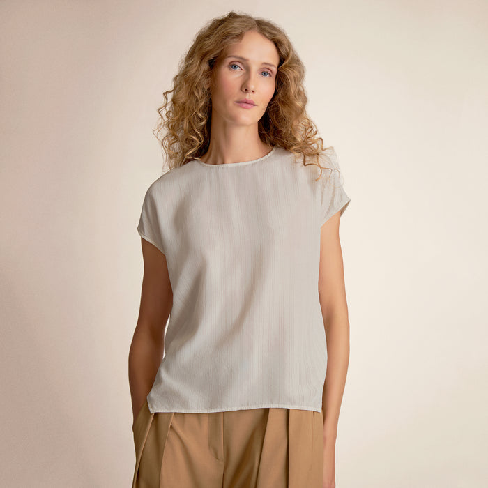 Woman wearing a light-colored top and beige pants against a plain background | Lead