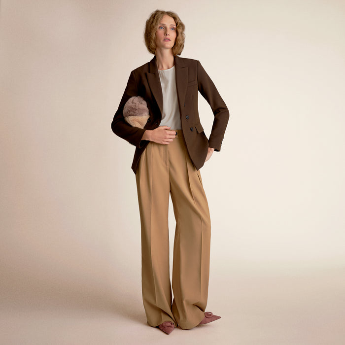 Woman wearing a brown blazer and beige pants on a beige background
