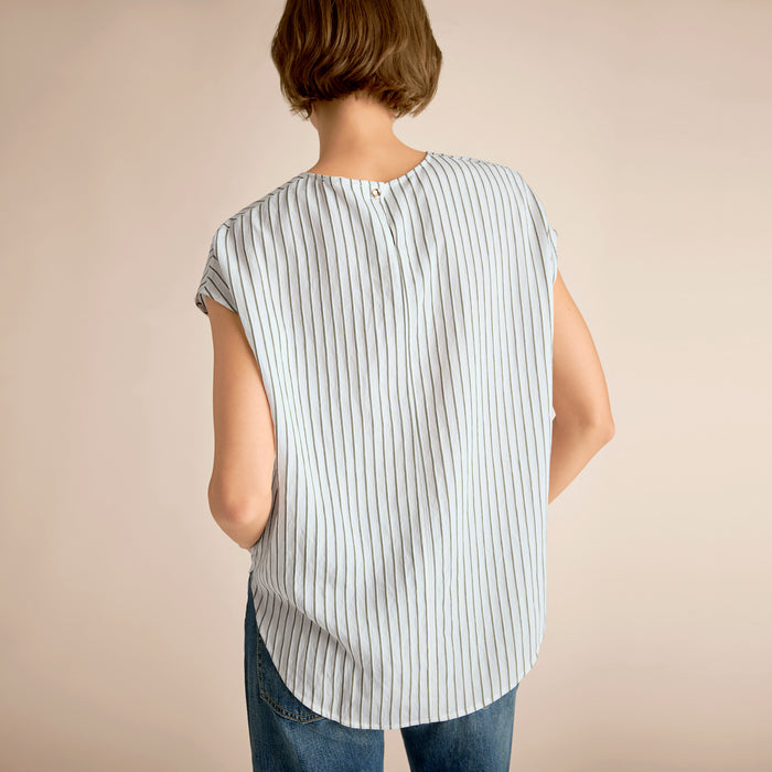 Person wearing a sleeveless striped shirt and jeans on a beige background