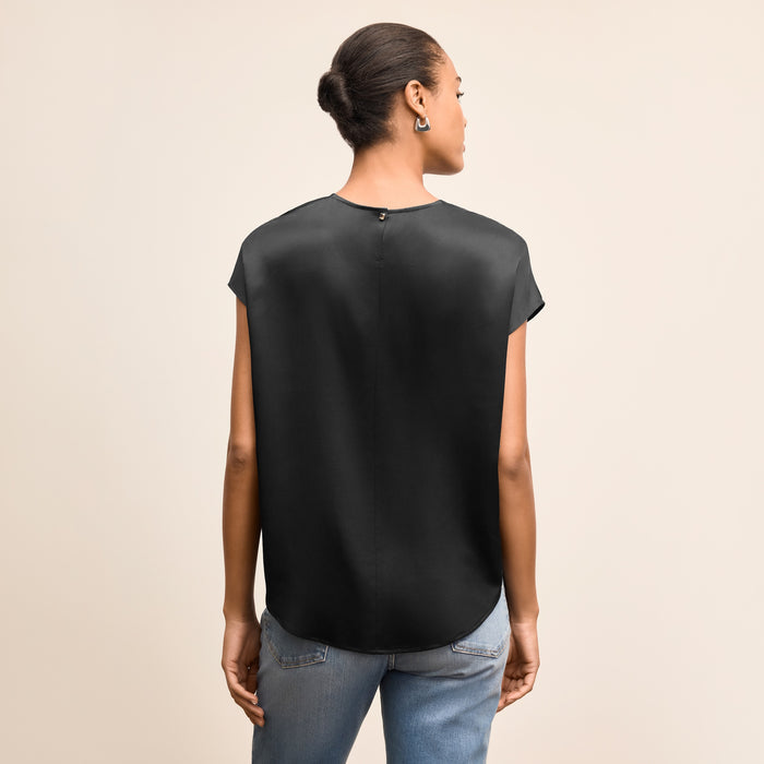 Person wearing a black sleeveless top and blue jeans on a beige background