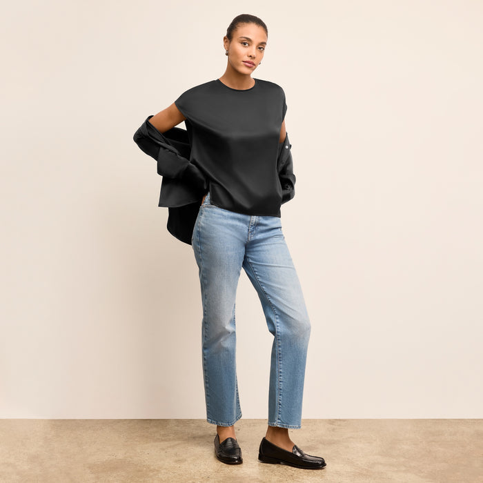 Woman wearing a black top and blue jeans against a beige background