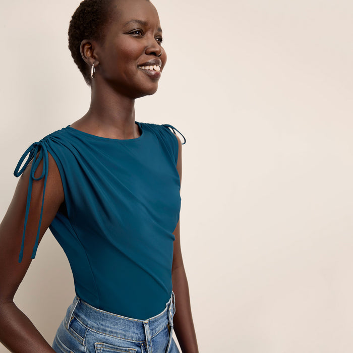 Woman wearing a teal top with tied sleeves against a beige background | Lead