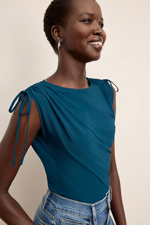 Woman wearing a blue top with tie sleeves against a beige background | Exclude | Grid