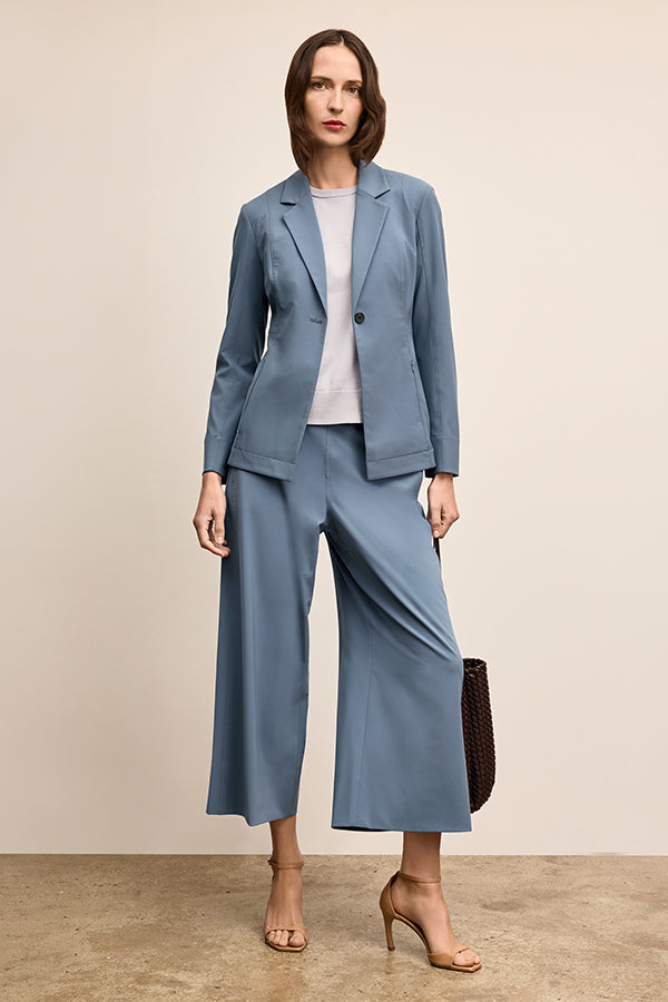 Woman wearing a blue suit with a white shirt, holding a brown handbag on a beige background | Grid Hover | Exclude