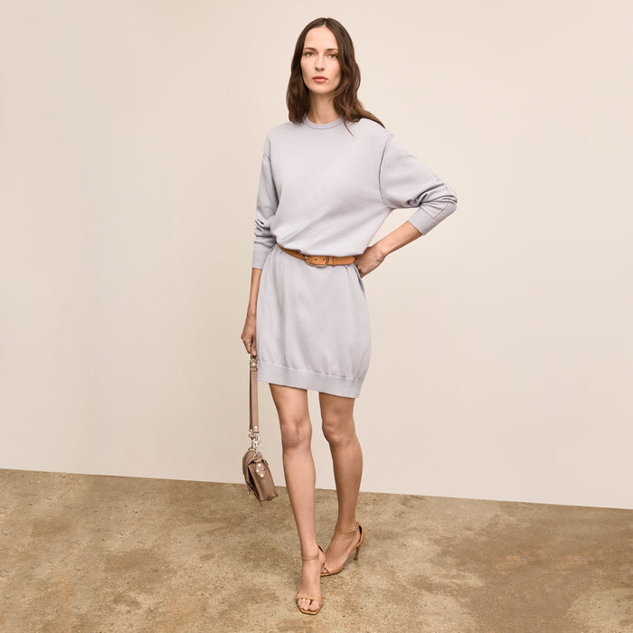 Woman wearing a light gray dress with a belt, standing against a plain background