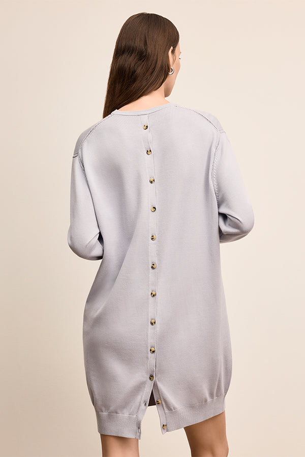 Woman wearing a light gray dress with button details on a beige background | Exclude | Grid Hover