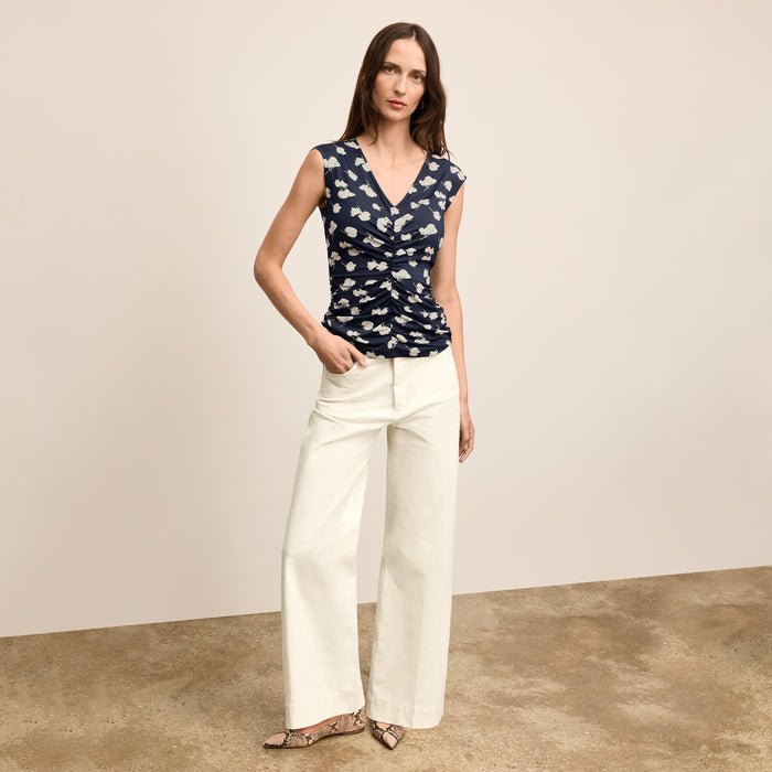 Woman wearing a navy floral top and white pants on a beige background