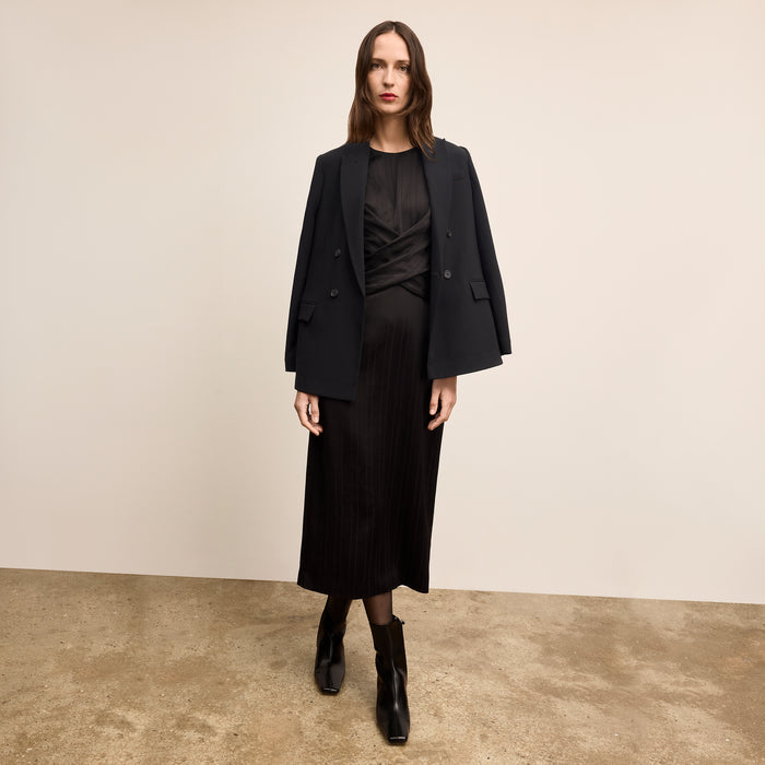 Woman wearing a black suit standing against a beige background
