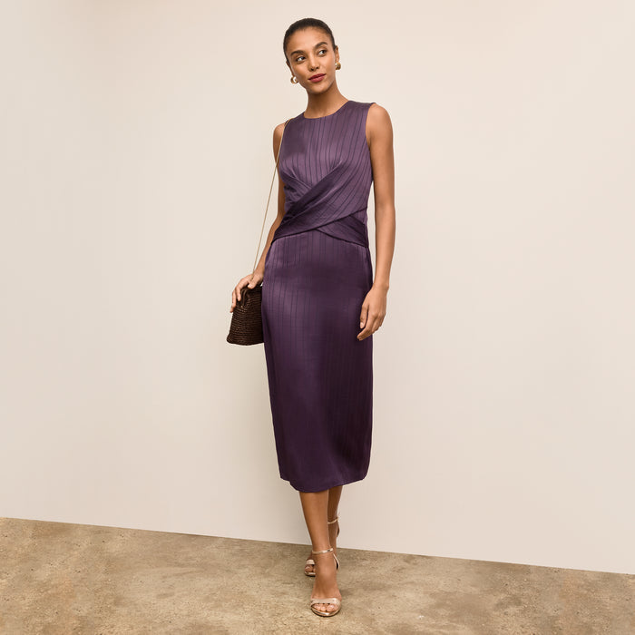 Woman wearing a purple dress holding a black handbag against a beige background | Lead