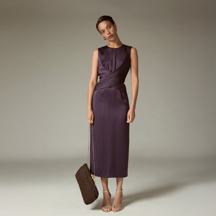 Woman wearing a purple dress holding a brown handbag against a neutral background