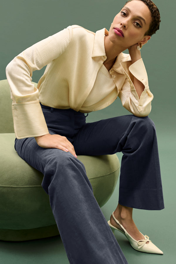 Woman sitting on a green chair wearing a beige blouse and navy pants. | ALT GRID | Exclude