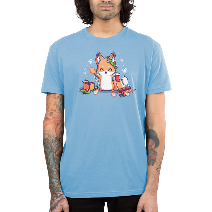 Premium Cotton T-shirt_TeeTurtle It's That Time of Year light blue t-shirt featuring a cheerful fox with green garland around its left ear surrounded by snowflakes and holding a red holiday stocking in one hand a Christmas cookie and a string of lights in the other. On the floor is red gift wrap, a red bow, Christmas cookies and a brown box on top of green gift wrap.
