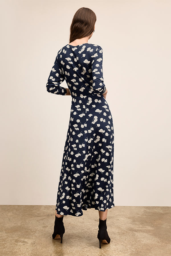 Woman wearing a navy dress with white floral pattern on a beige background | Exclude