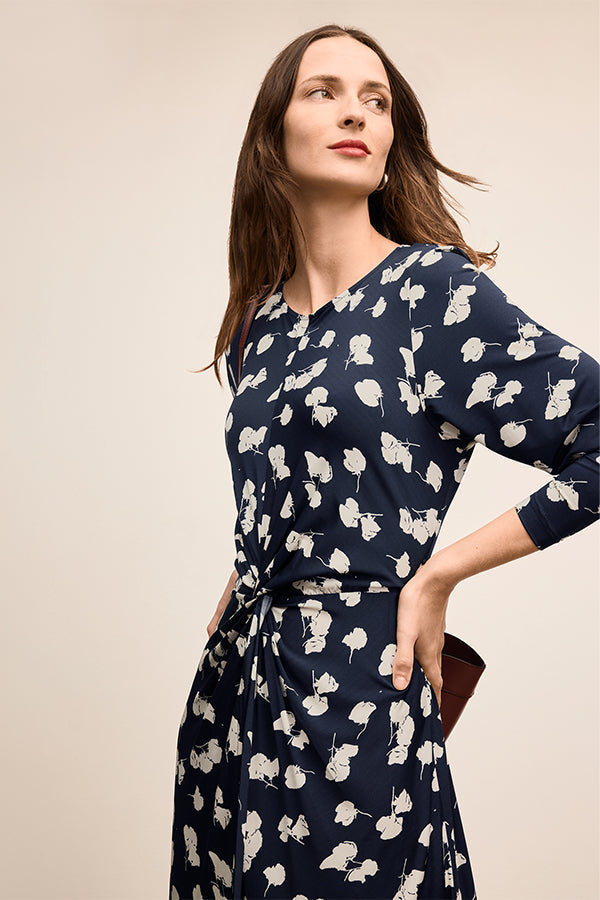 Woman wearing a navy blue dress with white floral pattern against a beige background | Exclude | Grid Hover