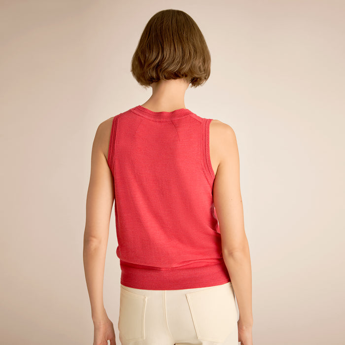 Person wearing a red sleeveless top and beige pants on a plain background