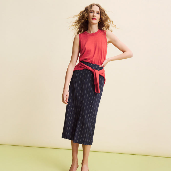 Woman wearing a red sleeveless top and navy pinstripe skirt on a yellow background