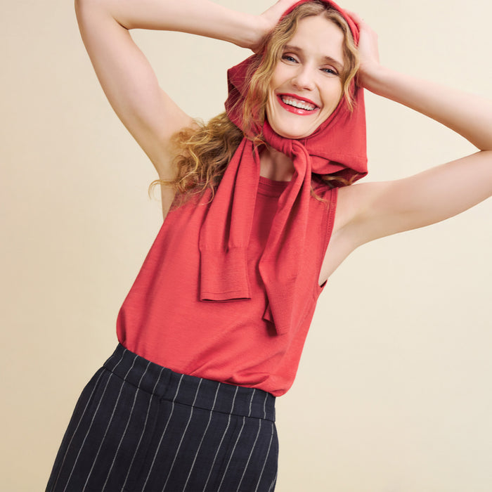 Woman wearing a red top and black pinstripe pants with a red scarf on a beige background
