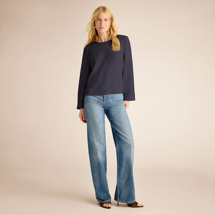 Woman wearing a navy sweater and blue jeans on a beige background | Lead