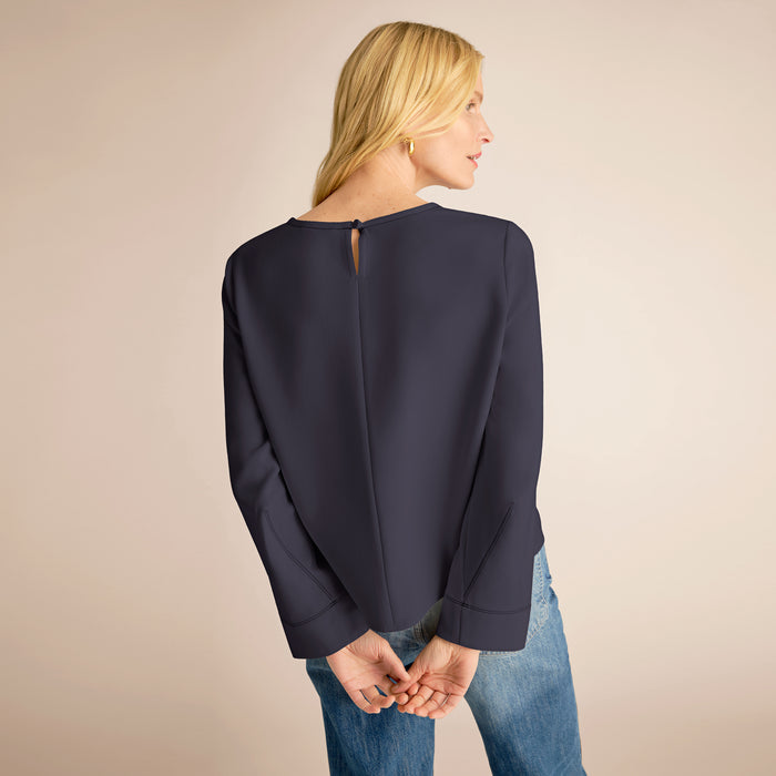 Woman wearing a navy blue blouse and blue jeans on a beige background