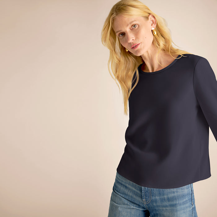 Woman wearing a navy sweater and blue jeans against a beige background