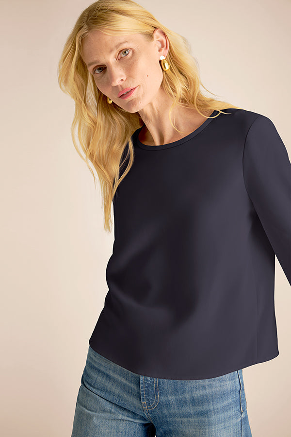 Woman wearing a navy blue long-sleeve top and blue jeans against a beige background | Exclude