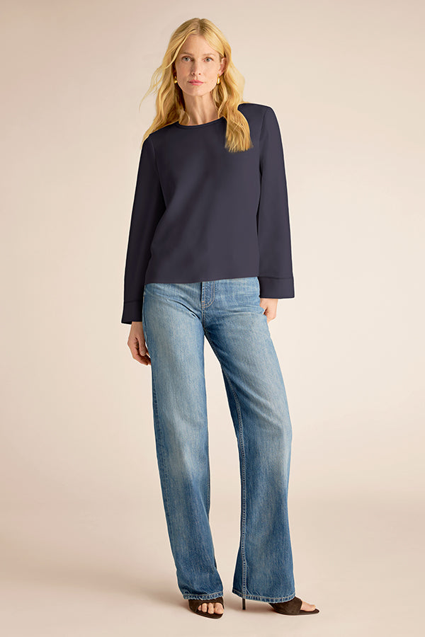 Woman wearing a navy sweater and blue jeans on a beige background | Exclude | Grid