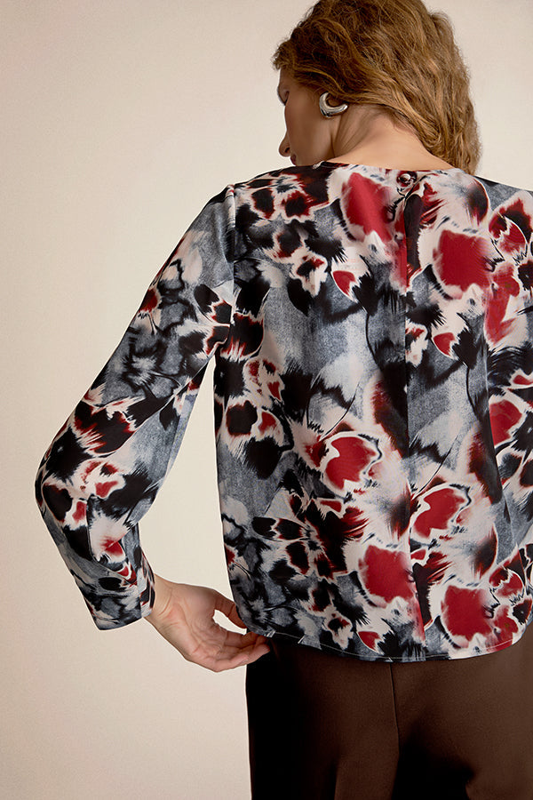 Person wearing a floral patterned blouse with red and black design on a plain background | Grid Hover | Exclude