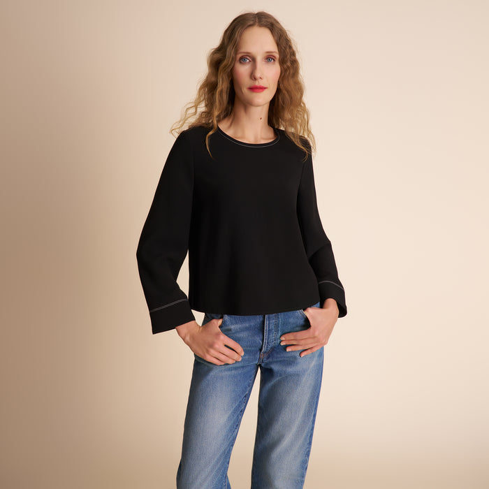 Woman wearing a black sweater and blue jeans against a beige background | Lead