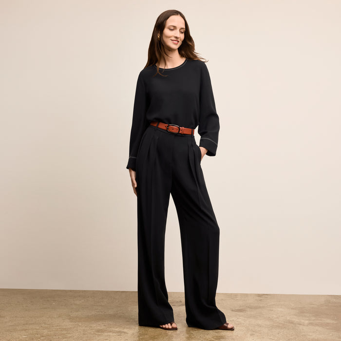Woman wearing a black outfit with a brown belt against a beige background
