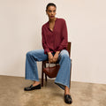 Woman sitting on a chair holding a brown handbag, wearing a red blouse and blue jeans | Lead