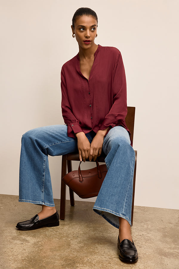 Woman sitting on a chair wearing a burgundy shirt, blue jeans, and black shoes, holding a brown handbag | Exclude