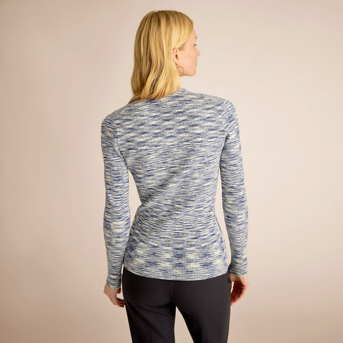 Woman wearing a blue and gray patterned long-sleeve top against a beige background