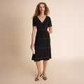 Woman wearing a black dress with white trim on a beige background | Lead