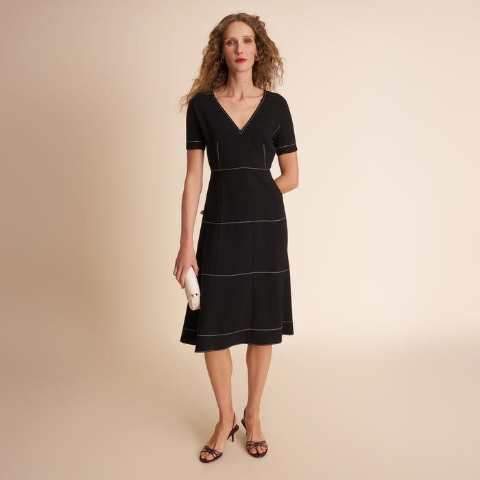 Woman wearing a black dress with white trim on a beige background | Lead