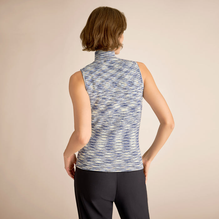 Woman wearing a sleeveless patterned top and dark pants on a beige background