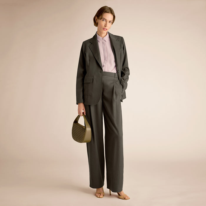 Woman in a gray suit holding a green handbag against a beige background