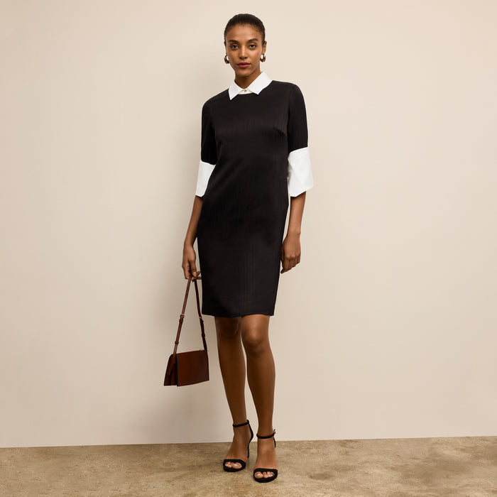 Woman wearing a black and white dress holding a brown handbag against a beige background