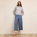 Woman wearing a light gray sweater and blue pants against a beige wall | Lead