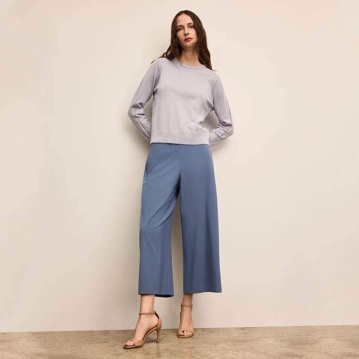 Woman wearing a light gray sweater and blue pants against a beige wall | Lead