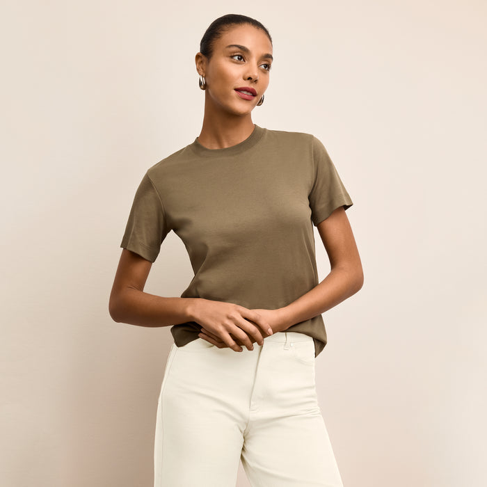 Woman wearing a green t-shirt and white pants against a beige background | Lead