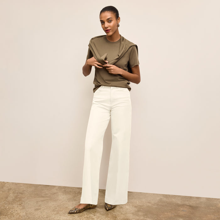 Woman wearing a green top and white pants against a plain background
