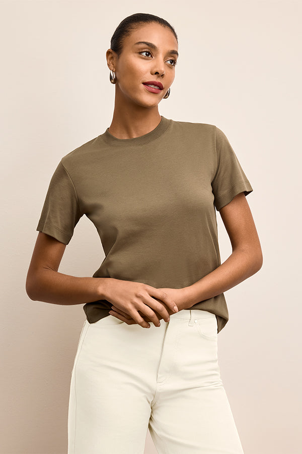 Woman wearing a green t-shirt and white pants against a beige background | Exclude | Grid