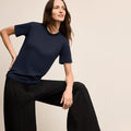 Woman wearing a navy blue top and black pants against a beige background | Lead