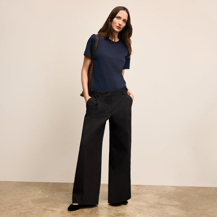Woman wearing a navy blue top and black wide-leg pants against a beige background
