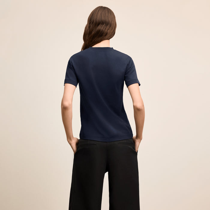 Person wearing a navy blue t-shirt and black pants on a beige background