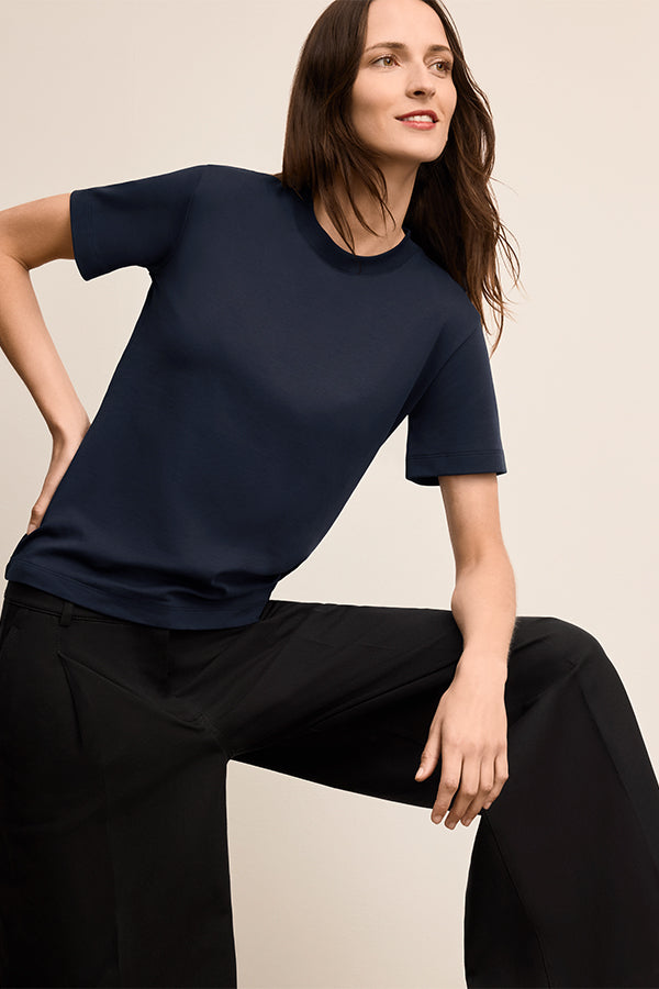 Woman wearing a navy blue top and black pants on a beige background | Exclude | Grid