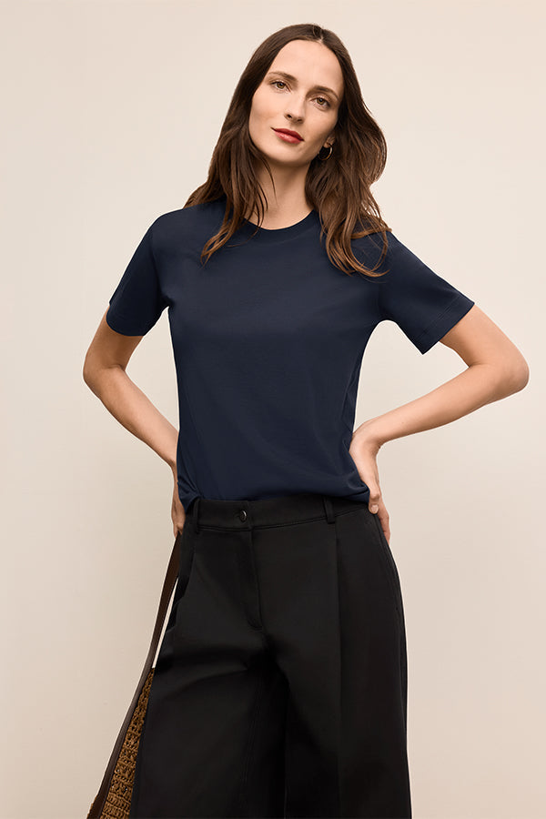 Woman wearing a navy blue t-shirt and black pants against a beige background | Exclude
